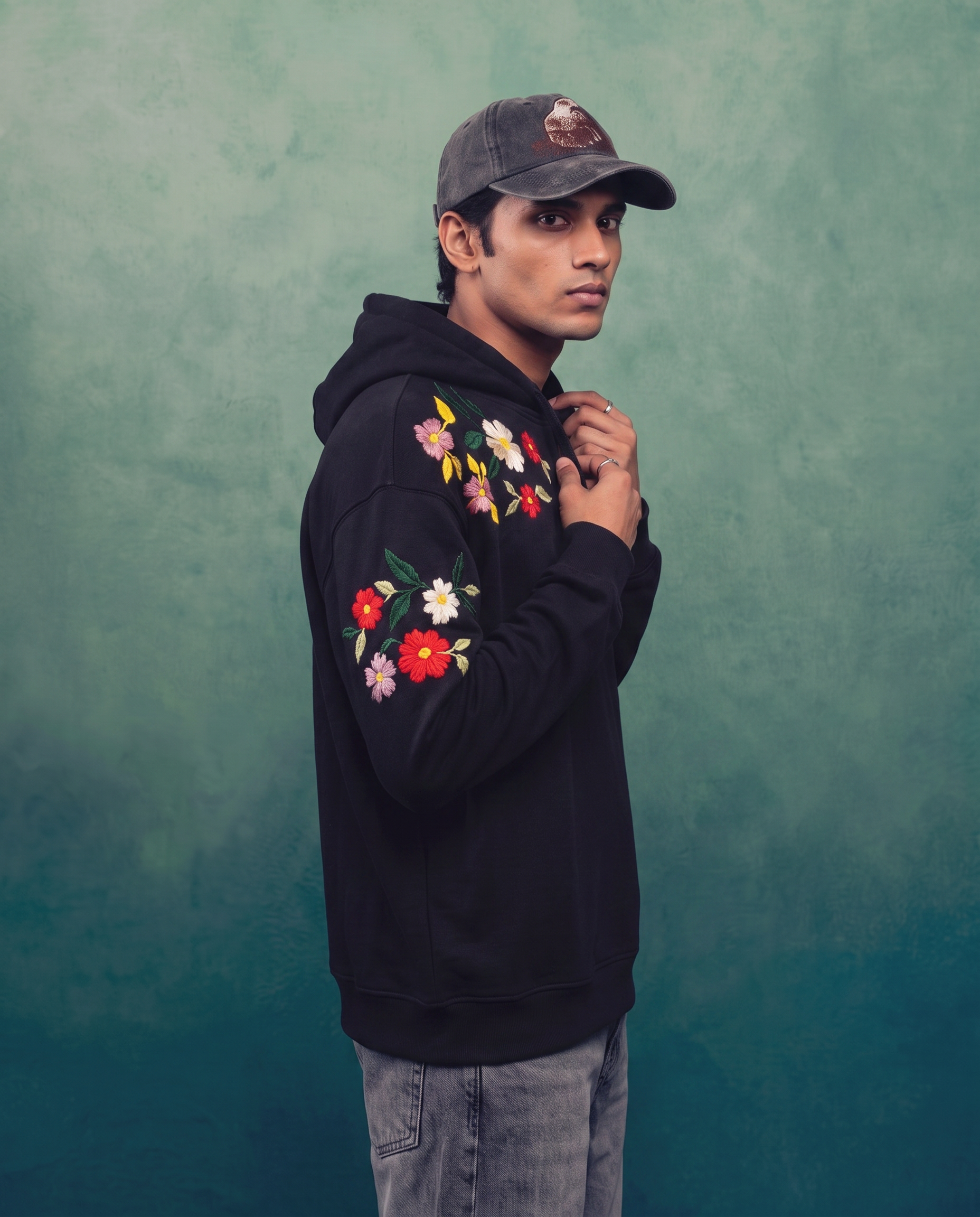 Side profile of a man in the black embroidered hoodie showing flowers along the shoulder and full sleeve