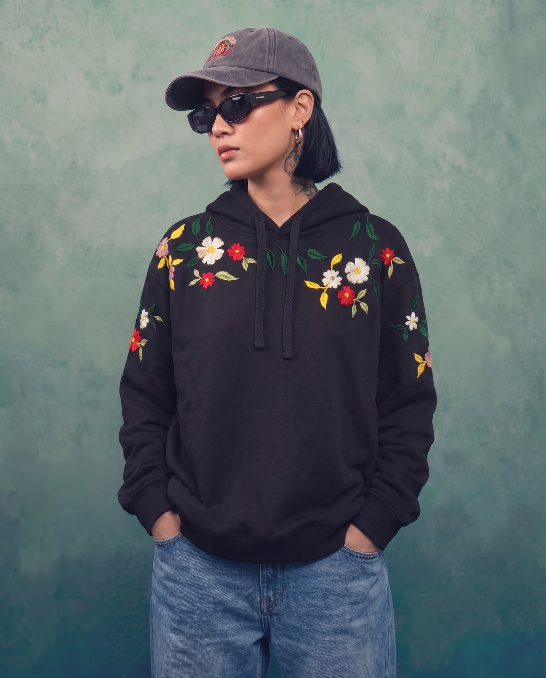 Woman in the black hand-embroidered floral hoodie with hands in the front pocket, shown with jeans