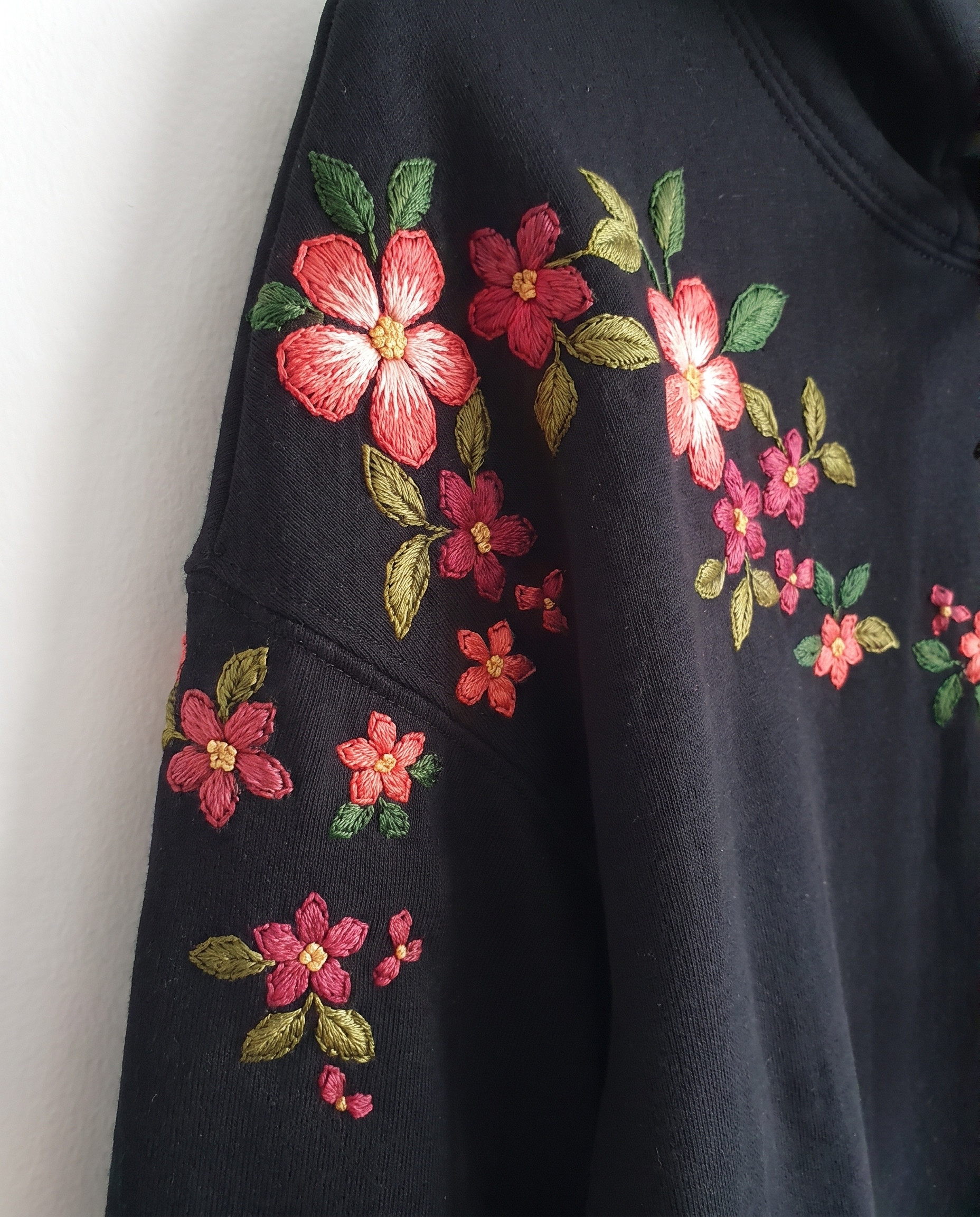 Shoulder and sleeve detail showing shaded coral petals and olive green leaves hand-stitched on black fleece