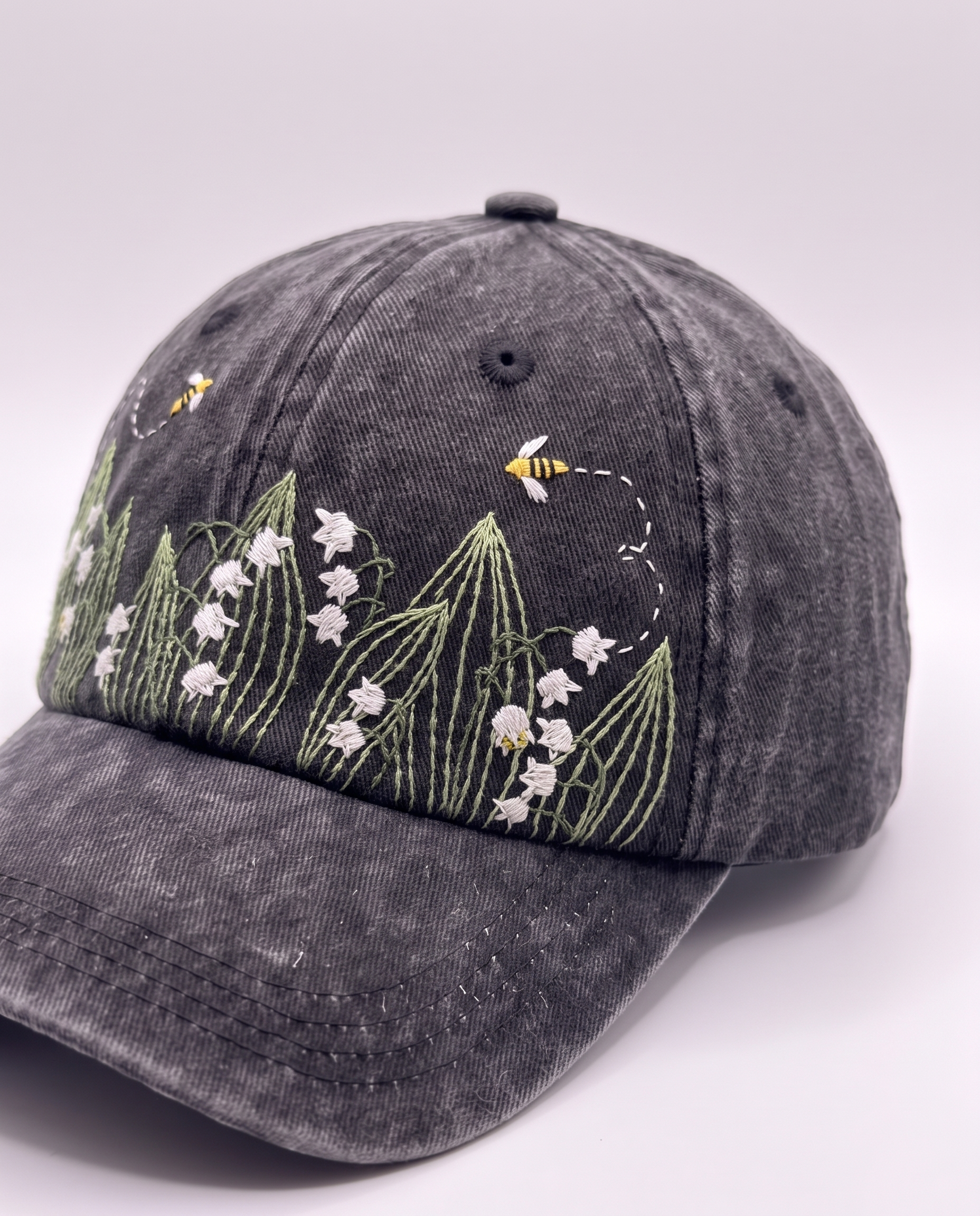 Close angle on the two stitched bees and their dashed flight paths curving up onto the crown of the cap