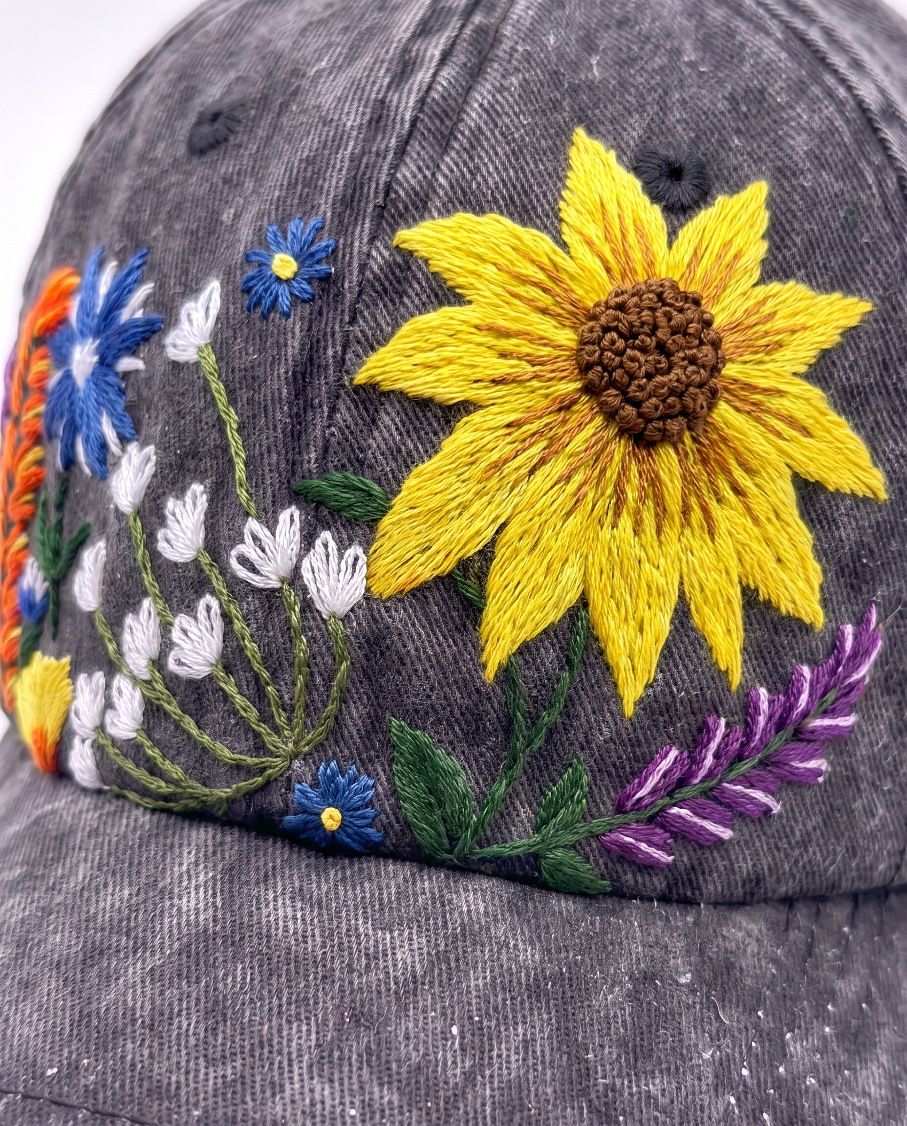 Detail crop of the wildflower embroidery: satin sunflower, blue cornflowers, white bells, lavender and an orange spike