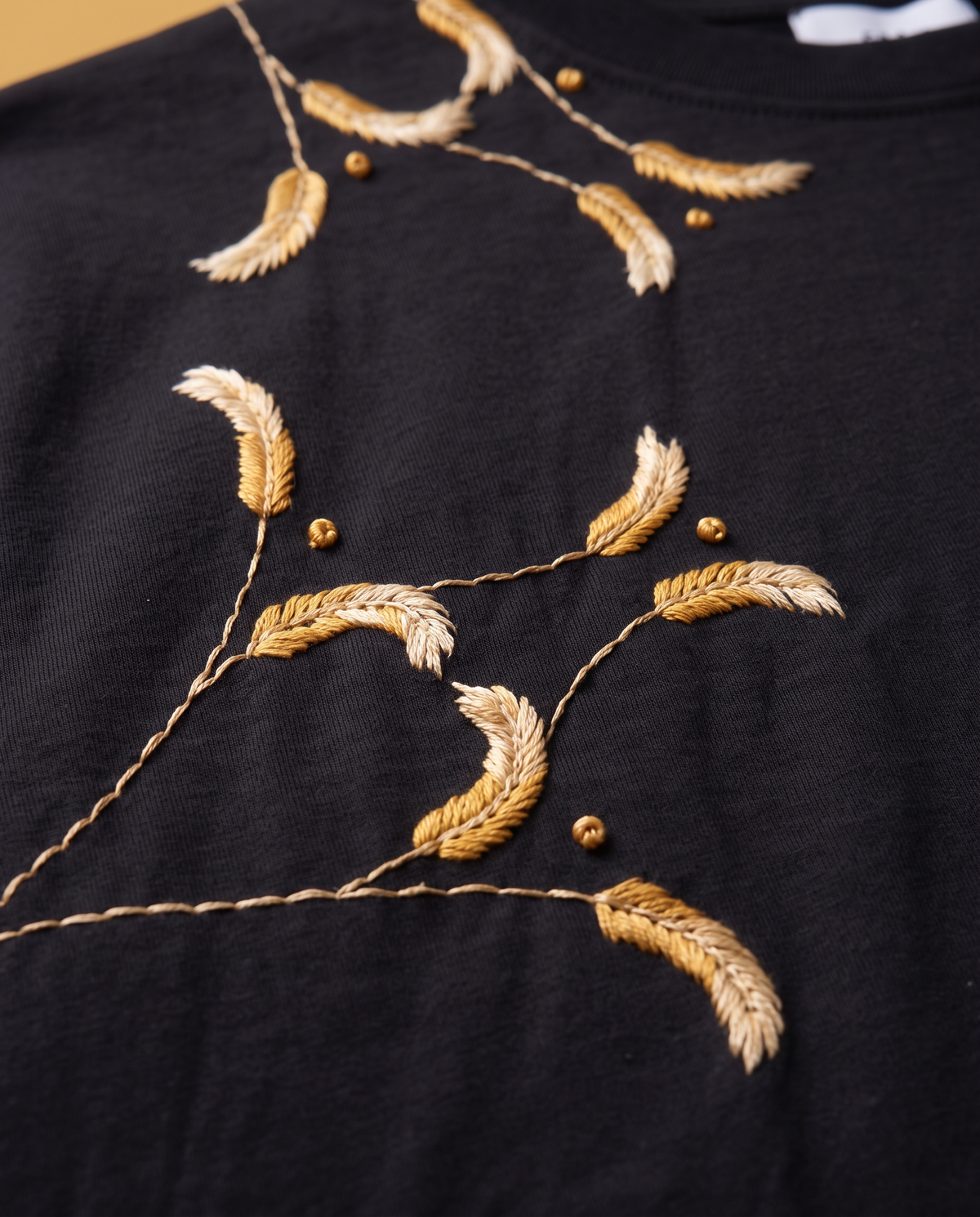 Close-up of fishbone-stitched wheat ears and twisted stem stitch on the Kanak black embroidered t-shirt