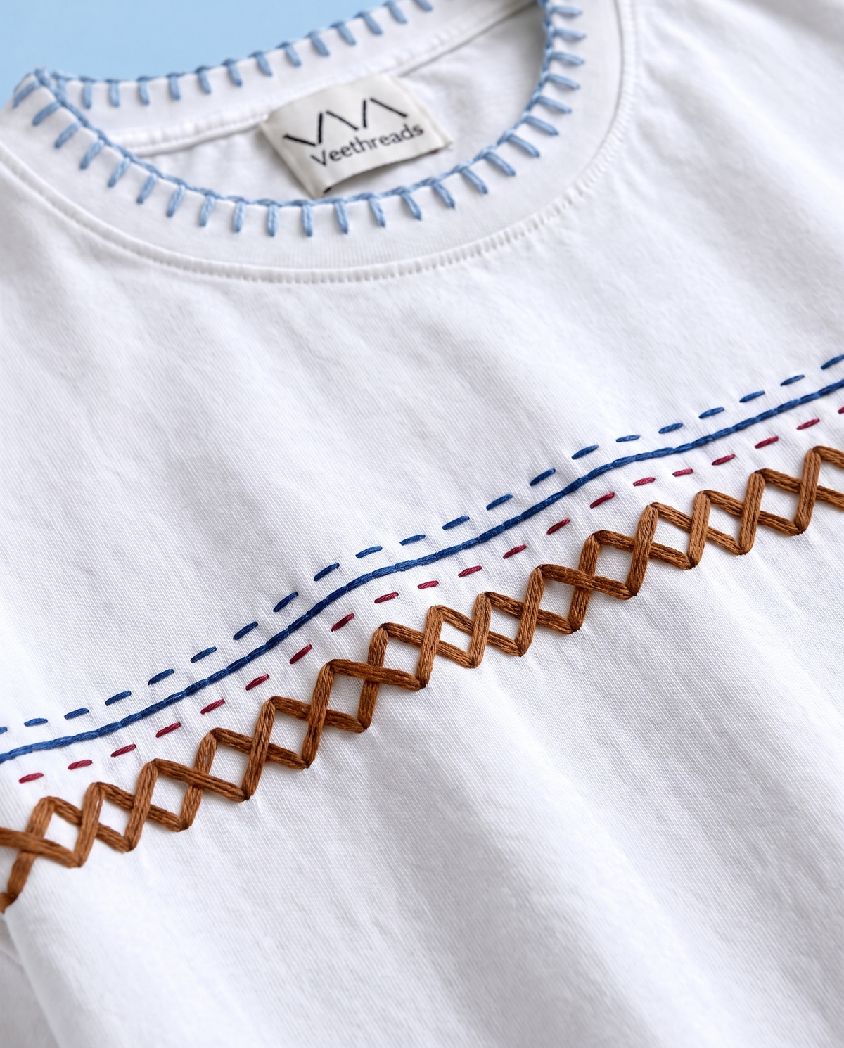 Close-up of kantha running stitch rows and brown herringbone embroidery on a white 220 GSM cotton tee