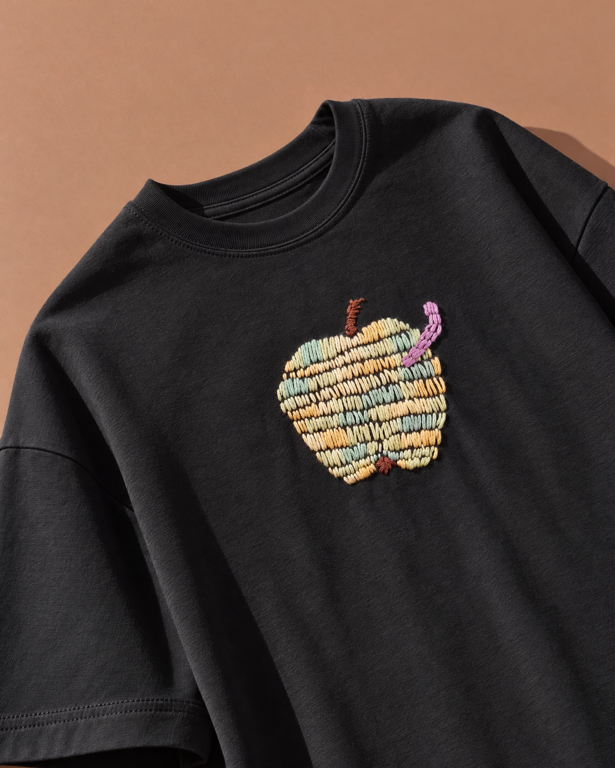 Black embroidered apple t-shirt, angled view of the centre-chest apple design