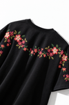 Floral embroidered t-shirt on white with a hand-stitched garland of coral and magenta flowers across the shoulders
