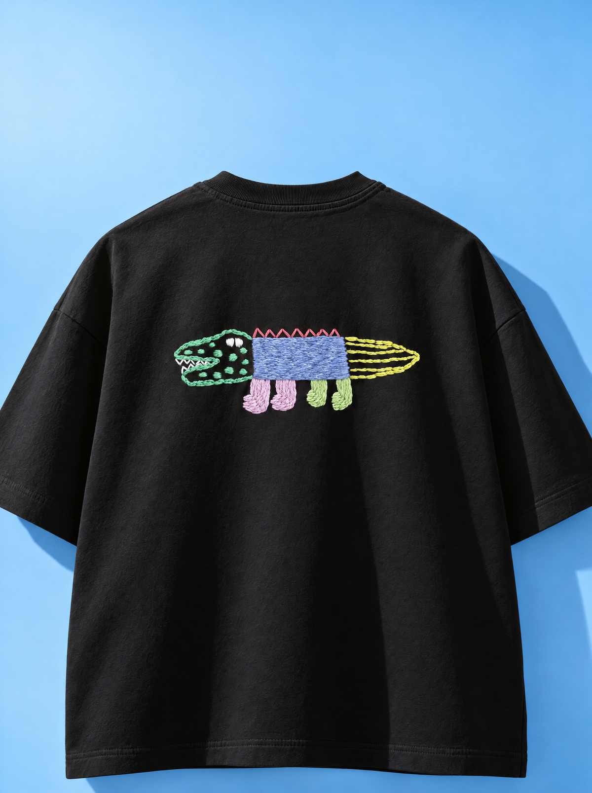 Black 220 GSM cotton oversized tee with a hand-stitched crocodile, full view on a blue background