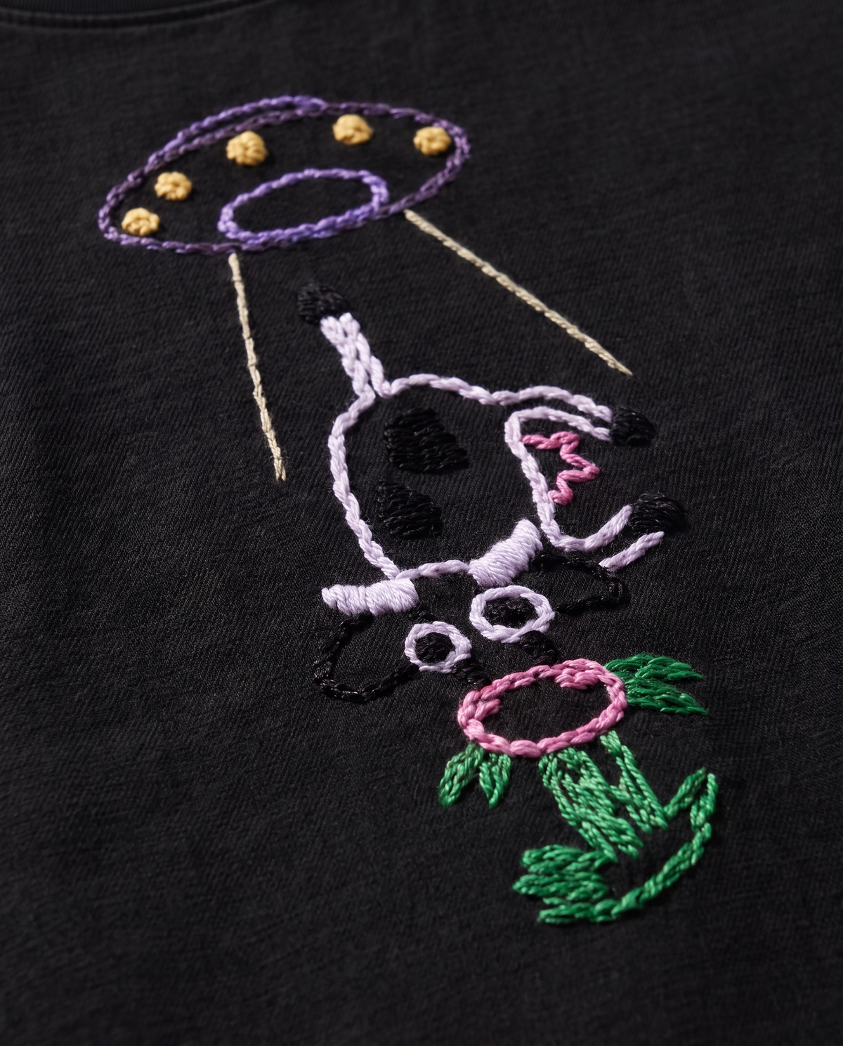 Close-up of the alien cow embroidery, purple UFO with yellow French knot lights, white chain-stitch cow and pink flower