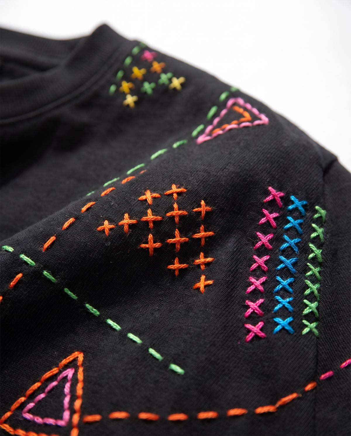 Close-up of cross stitch clusters, running stitch lines and stitched triangles on a black cotton tee