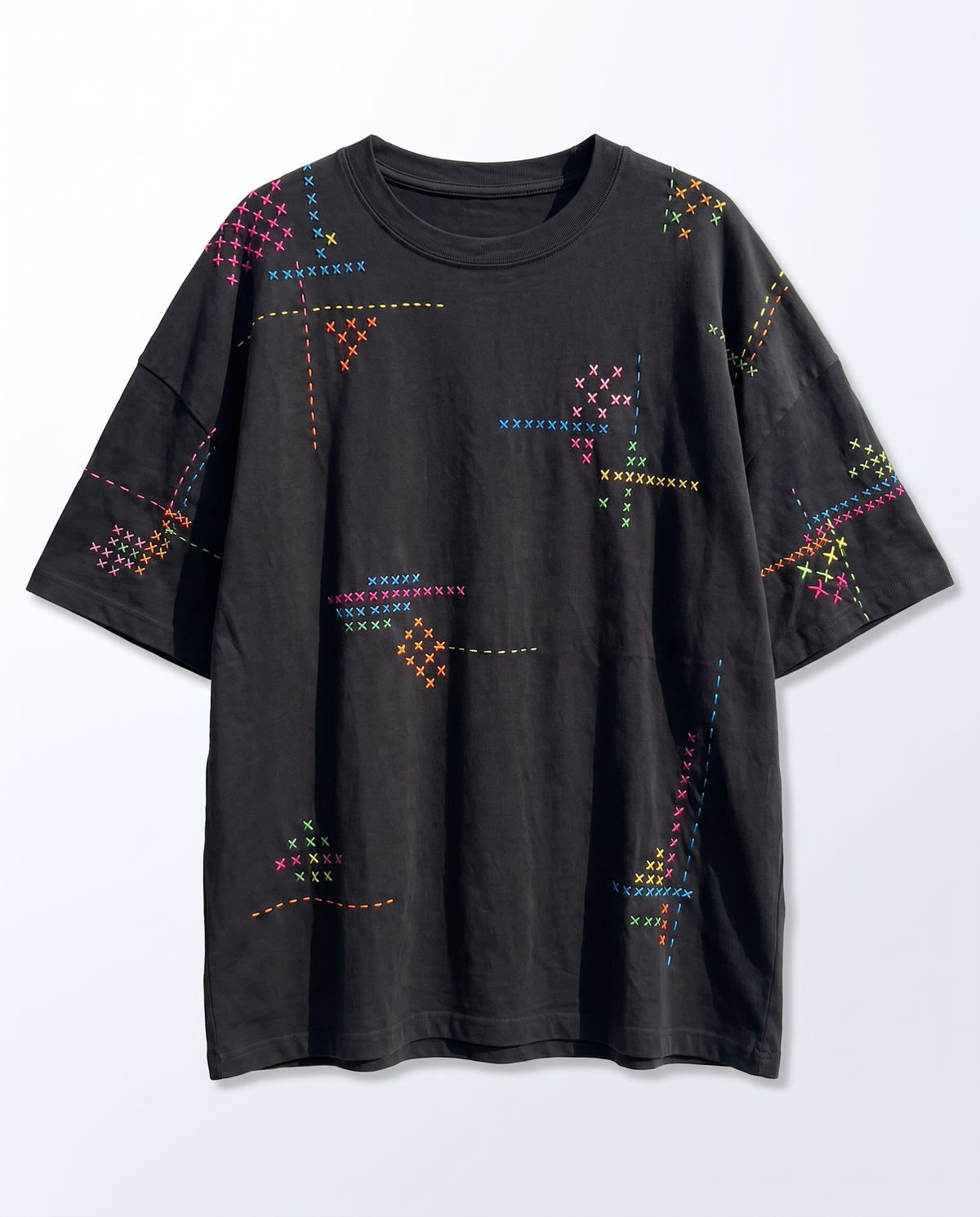 Black oversized t-shirt laid flat with all-over pink, blue, orange, yellow and green cross stitch embroidery