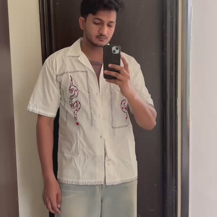Close-up of a cream cotton shirt with hand-embroidered red heart and black snake motifs, showcasing detailed Indian-inspired craftsmanship and bold contrast stitching. 