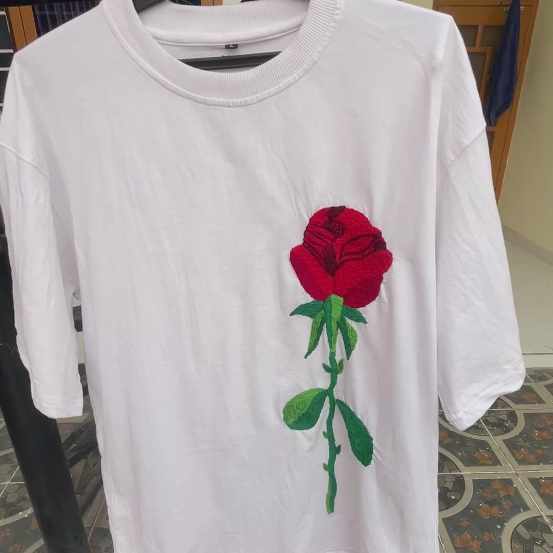 Man wearing a black oversized t-shirt with a large hand-embroidered red rose and green stem design on the front.